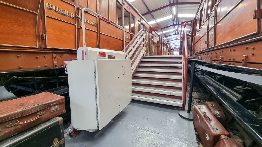 Image shows the stair lift inside the Vintage Carriages Trust museum. The lift is on the left side of the stairs and takes you onto the carriage viewing platform.